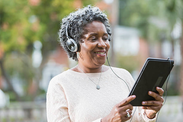 Woman wearing headphones and using a digital tablet listening to an audio book.