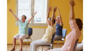 A group of people sitting on chairs taking part in gentle exercise.