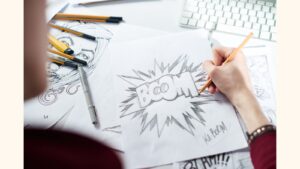 A person drawing with a pencil on a sheet of white paper. The word 'BOOM' is at the center of the page.