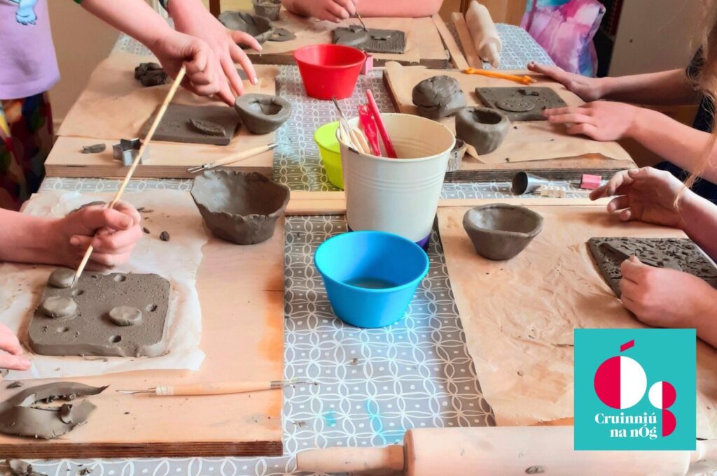 A photograph of small hands creating clay pots and artwork on a wooden table.