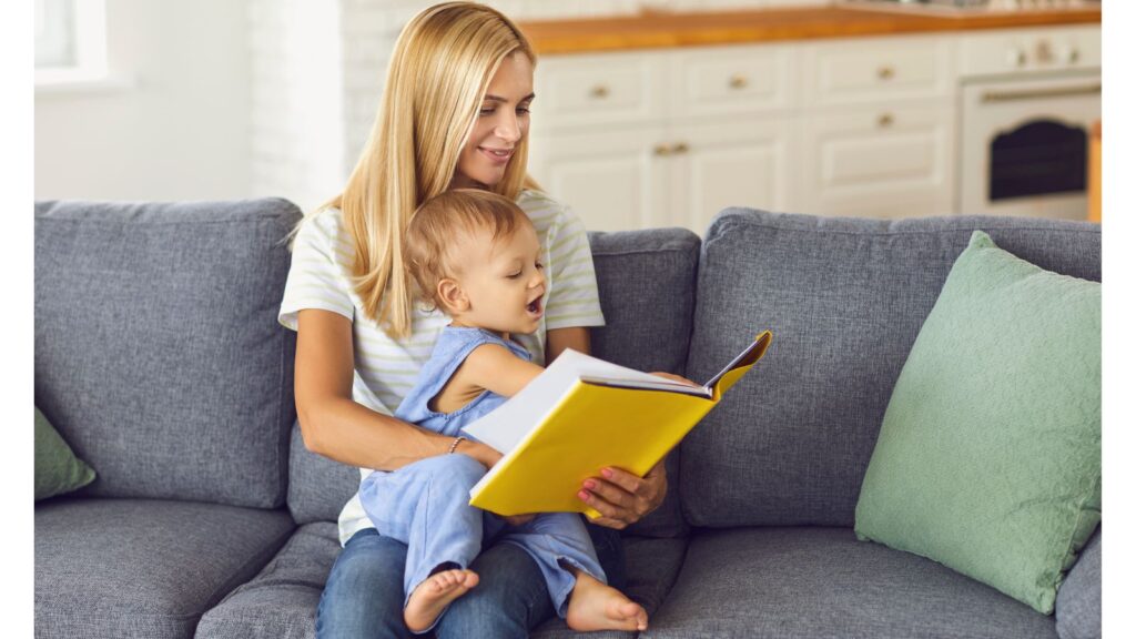 A child sitting on an adults knee looking at a book with a yellow cover.